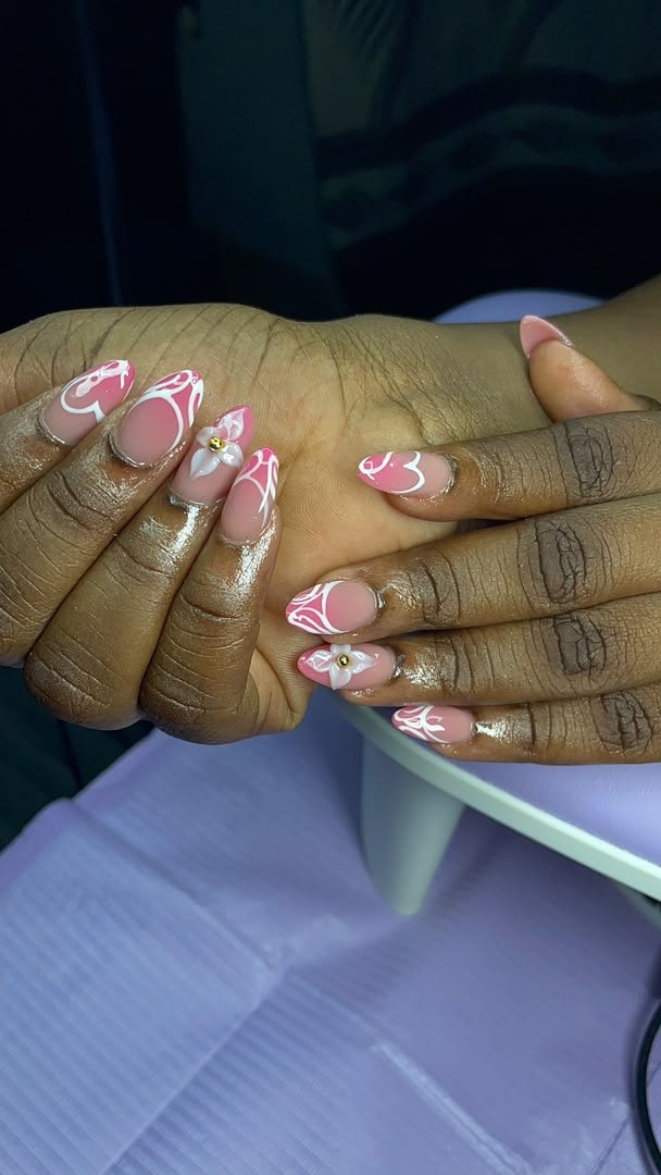 Pink almond nails with white swirl art and a 3D flower with a gold stud